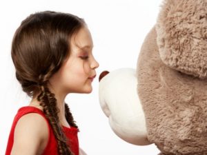 Portrait of a little brunette girl kissing a teddy bear into it's nose isolated on white background, close up